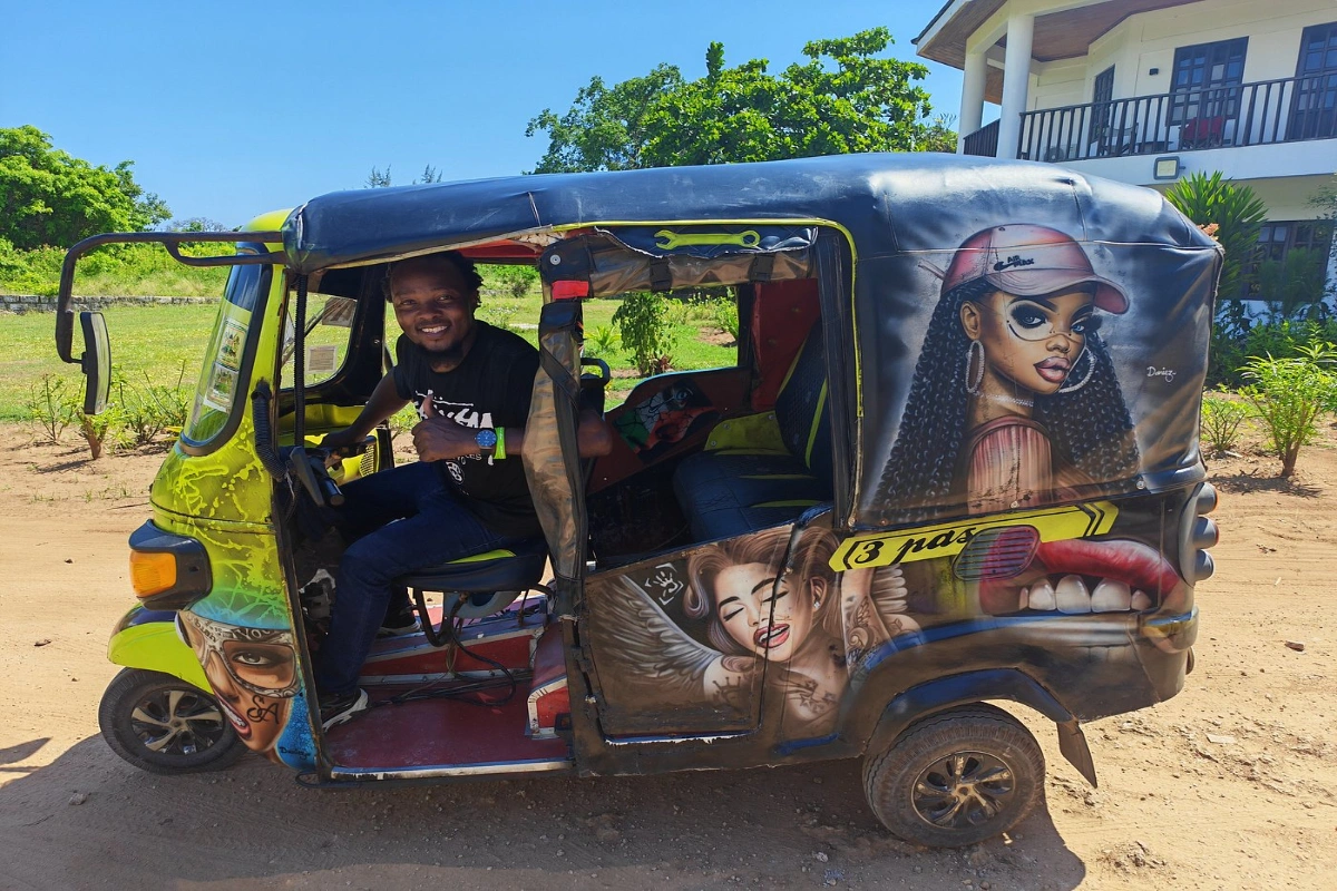 A colorful local auto-rickshaw tuk-tuk driving along the palm-lined Diani Beach Road in Kenya